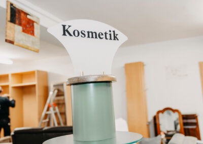 Ein Schild mit der Aufschrift "Kosmetik" steht auf einem Podest in einem Raum.